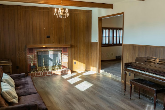 living room with a chandelier, wooden walls, dark hardwood / wood-style floors, beamed ceiling, and a fireplace