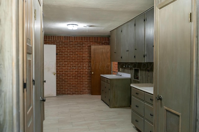 interior space with brick wall, sink, gray cabinetry, and a textured ceiling