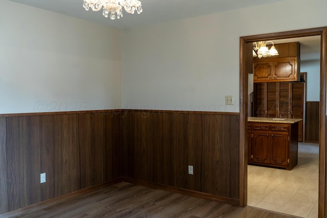 spare room featuring light wood-type flooring, an inviting chandelier, and wood walls