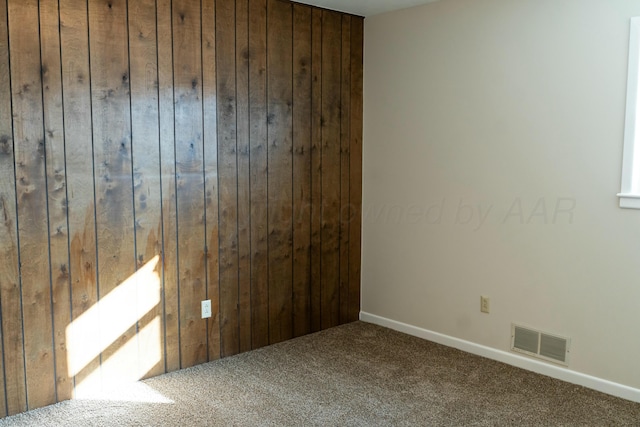 carpeted empty room featuring wood walls