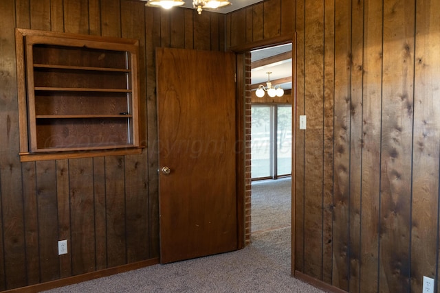 corridor featuring an inviting chandelier, wooden walls, and light carpet