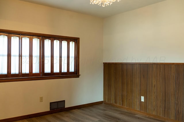 unfurnished room with baseboards, a notable chandelier, visible vents, and wood finished floors