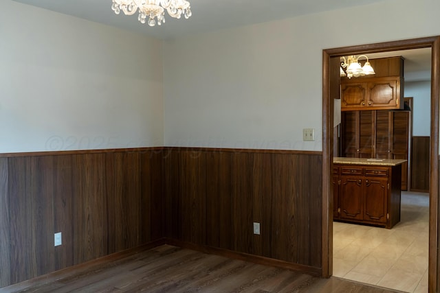 spare room featuring wood walls, a notable chandelier, wainscoting, and light wood finished floors