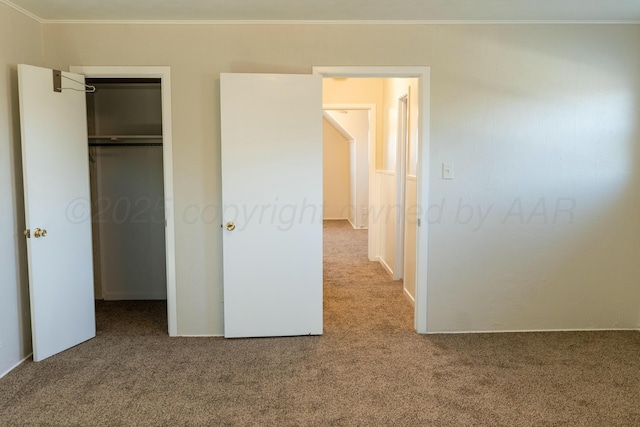 unfurnished bedroom with carpet flooring, a spacious closet, ornamental molding, and a closet