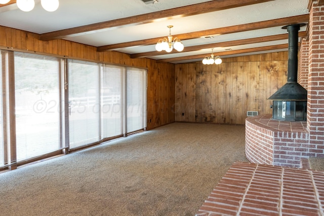 unfurnished living room with beam ceiling, wooden walls, carpet, and a wood stove