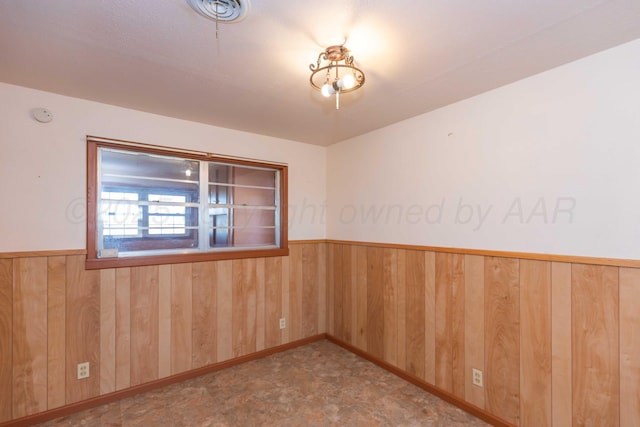 empty room featuring a wainscoted wall and wooden walls