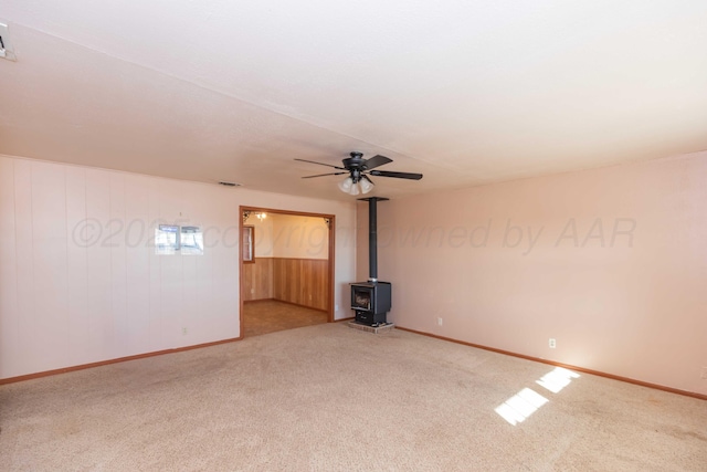 unfurnished living room with visible vents, a wood stove, carpet flooring, ceiling fan, and baseboards