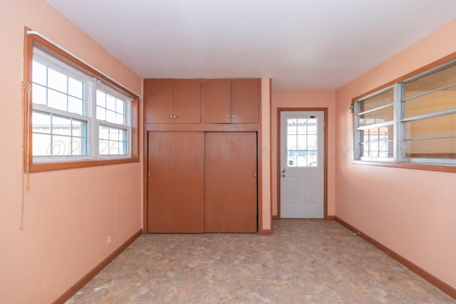 unfurnished bedroom with light floors, multiple windows, a closet, and baseboards