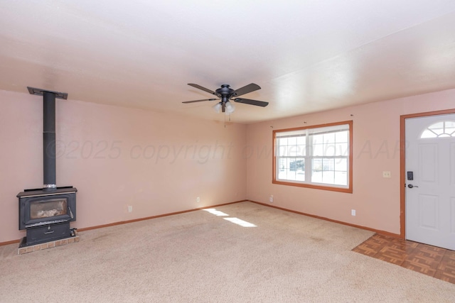 unfurnished living room with a ceiling fan, carpet flooring, a wood stove, and baseboards