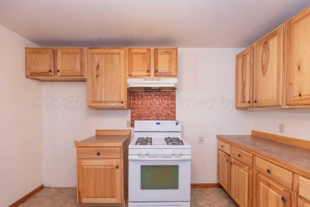 kitchen with under cabinet range hood, white gas range, baseboards, and backsplash