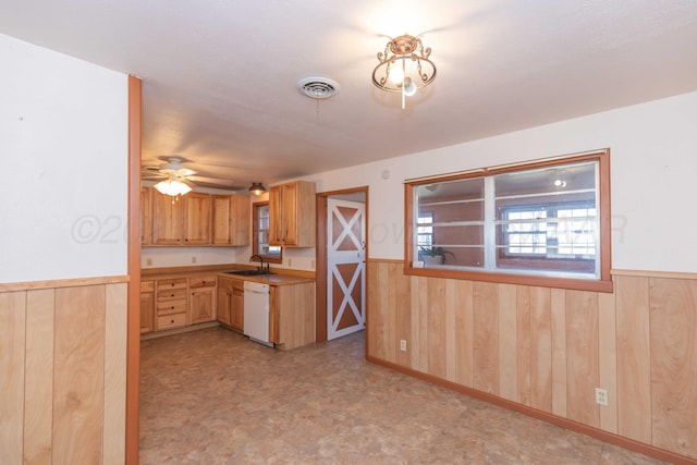 kitchen featuring wood walls, a sink, visible vents, wainscoting, and dishwasher