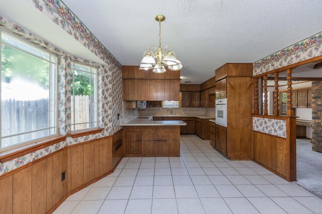 6111 Princeton St, Amarillo, TX 79109 - kitchen featuring wallpapered walls, brown cabinets, white oven, a peninsula, and a chandelier
