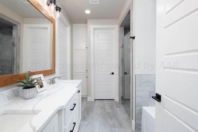 full bath featuring double vanity, a shower stall, recessed lighting, and a sink