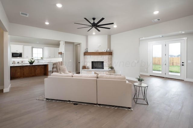 living area featuring visible vents, a fireplace, baseboards, ceiling fan, and light wood-style flooring