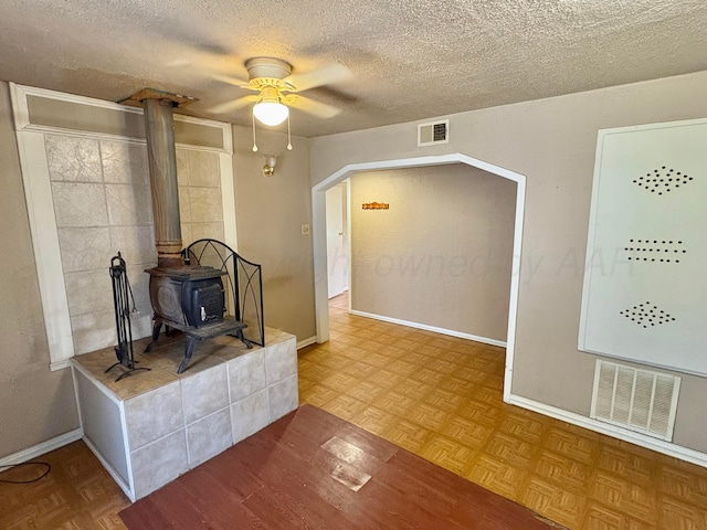 605 E 4th St, Panhandle, TX 79068 - living room featuring a ceiling fan, a textured ceiling, a wood stove, baseboards, and parquet flooring