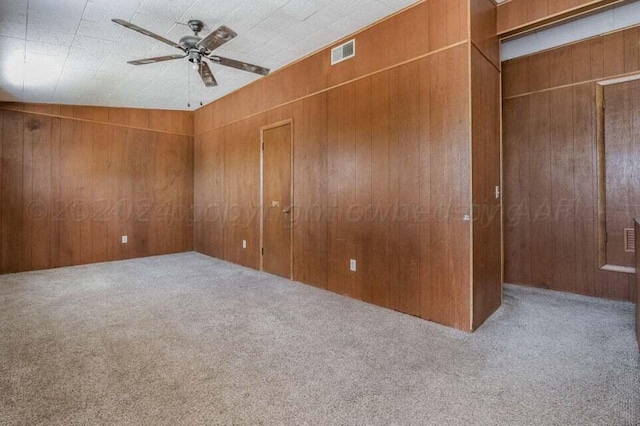 carpeted empty room with visible vents, wooden walls, and a ceiling fan
