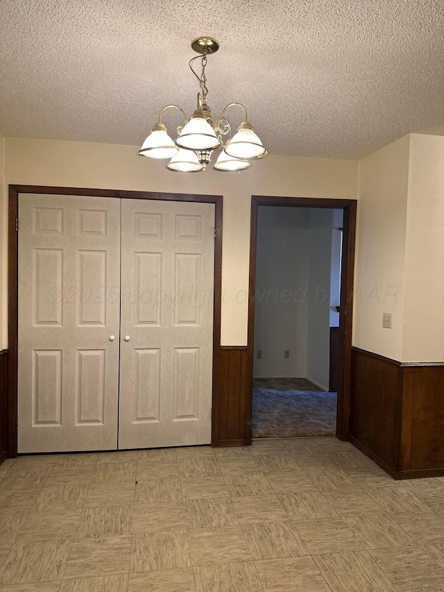 unfurnished bedroom with wood walls, a textured ceiling, a closet, and a notable chandelier