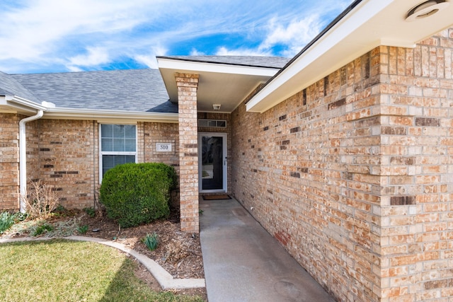 view of exterior entry with brick siding and a shingled roof