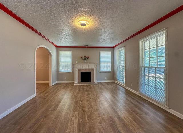 unfurnished living room with plenty of natural light, crown molding, a fireplace, and wood finished floors