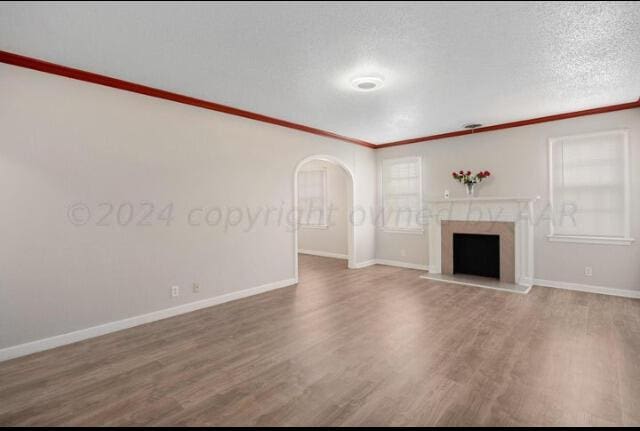 unfurnished living room with arched walkways, a premium fireplace, wood finished floors, a textured ceiling, and crown molding