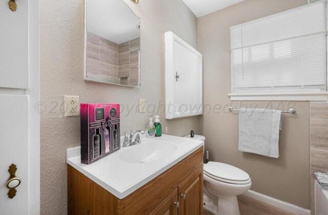 bathroom featuring toilet, baseboards, a bath, and vanity