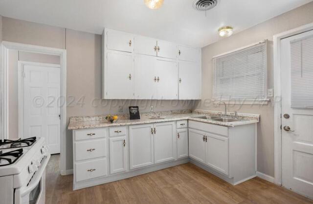 kitchen featuring white range with gas stovetop, visible vents, white cabinets, light wood-style flooring, and a sink