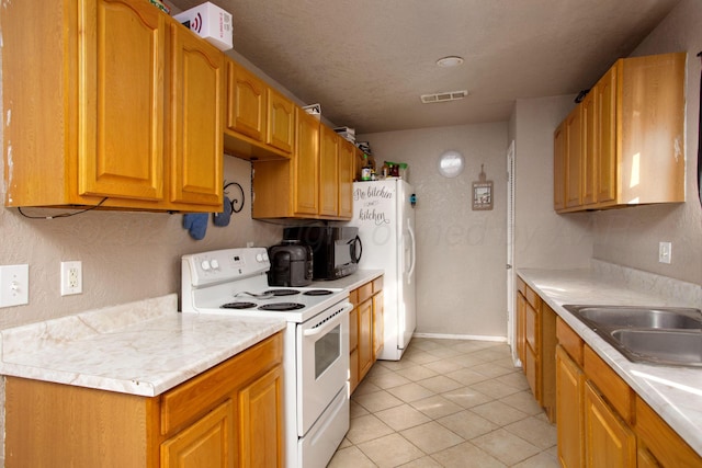 kitchen with light tile patterned floors, white appliances, sink, and a textured ceiling