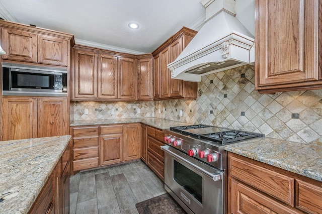 7402 Lynnlee Pl, Amarillo, TX 79121 - kitchen with custom range hood, appliances with stainless steel finishes, brown cabinetry, light wood finished floors, and light stone counters