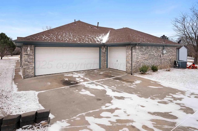 exterior space featuring roof with shingles, brick siding, an attached garage, central AC unit, and driveway