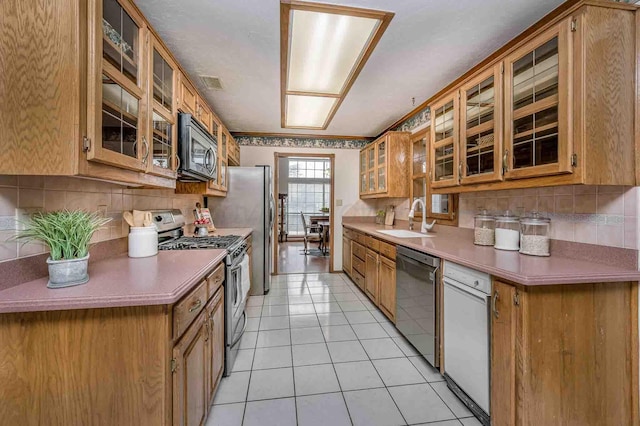 kitchen featuring brown cabinetry, decorative backsplash, glass insert cabinets, stainless steel appliances, and a sink