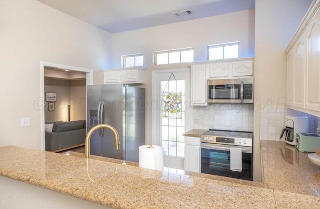 kitchen with a high ceiling, white cabinetry, appliances with stainless steel finishes, and backsplash