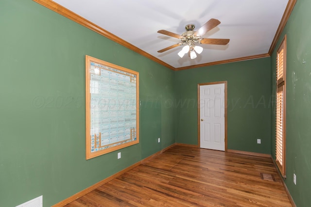 empty room featuring crown molding, baseboards, visible vents, and wood finished floors