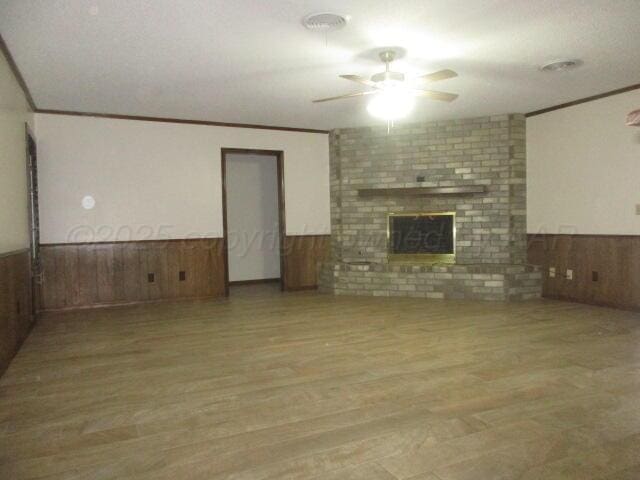 unfurnished living room featuring wood-type flooring, wood walls, crown molding, ceiling fan, and a fireplace