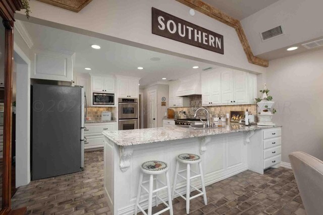 2200 Parker St, Amarillo, TX 79109 - kitchen featuring stainless steel appliances, a peninsula, a sink, white cabinets, and premium range hood