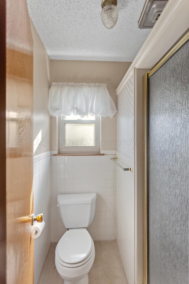 bathroom with a textured ceiling, toilet, a shower with door, and tile walls