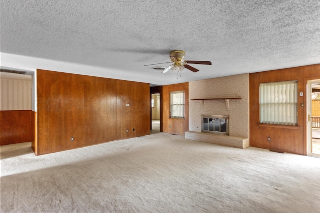 unfurnished living room featuring light carpet, a textured ceiling, ceiling fan, wooden walls, and a fireplace