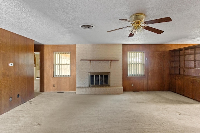 unfurnished living room with light carpet, a textured ceiling, ceiling fan, wooden walls, and a fireplace