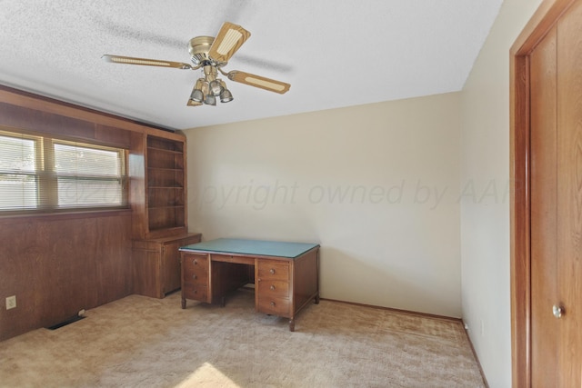 unfurnished office featuring light carpet, a textured ceiling, ceiling fan, and wooden walls