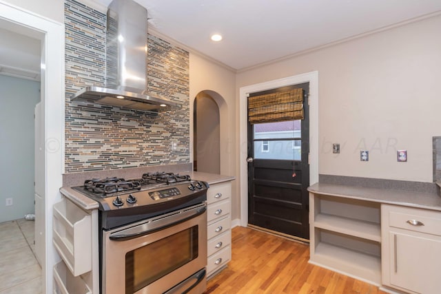 kitchen with white cabinetry, wall chimney exhaust hood, stainless steel gas range, decorative backsplash, and ornamental molding