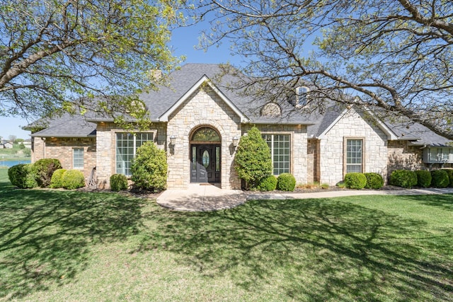 view of front facade with stone siding, roof with shingles, and a front yard