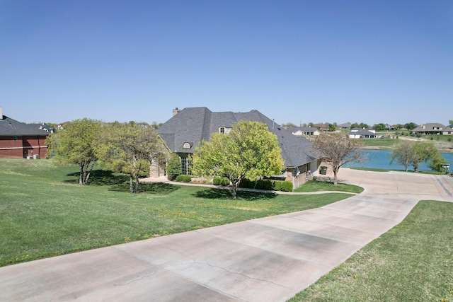 view of front of property featuring a chimney, a front yard, a water view, and concrete driveway