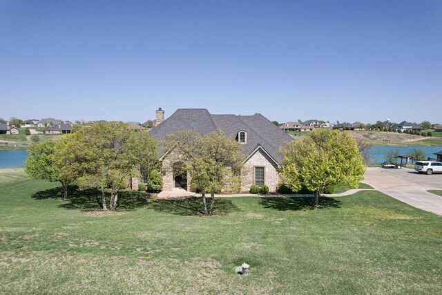 view of front of property with a chimney, a water view, stone siding, a front yard, and a residential view