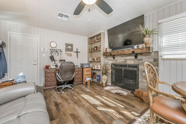office with built in shelves, hardwood / wood-style floors, ceiling fan, and a stone fireplace
