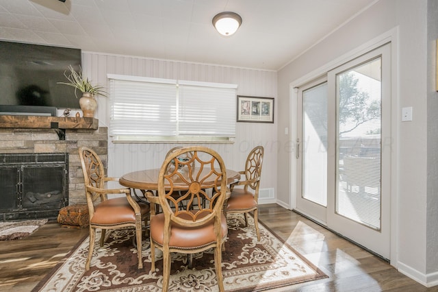 dining area featuring a stone fireplace, hardwood / wood-style flooring, and crown molding