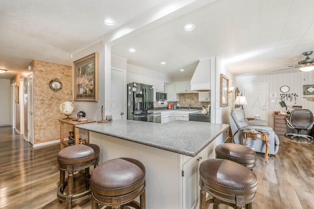 kitchen featuring stainless steel appliances, white cabinetry, a kitchen bar, hardwood / wood-style flooring, and kitchen peninsula