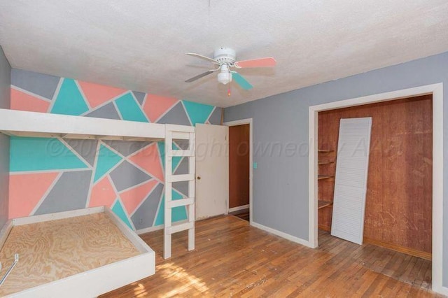 unfurnished bedroom featuring ceiling fan, a textured ceiling, baseboards, and hardwood / wood-style floors