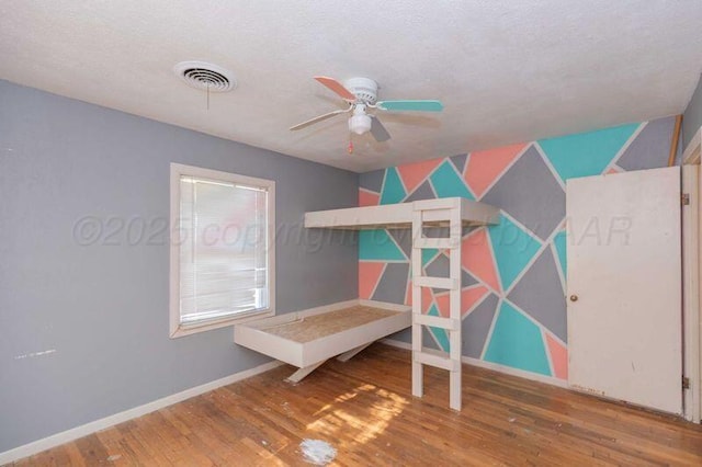 bedroom with visible vents, a textured ceiling, baseboards, and wood finished floors