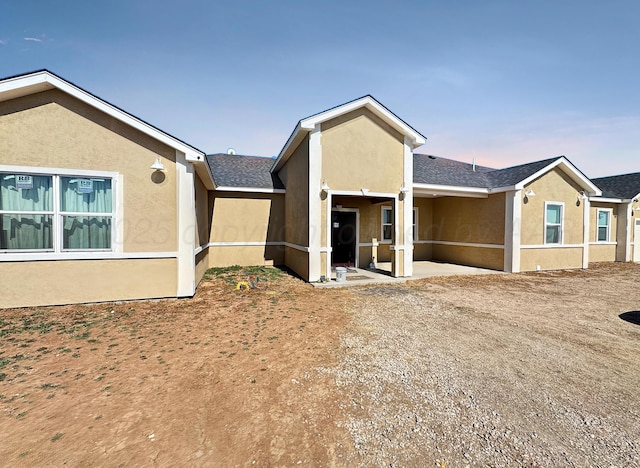 view of front of home with a patio area, roof with shingles, and stucco siding