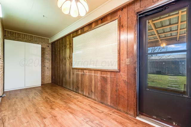 unfurnished bedroom featuring wood finished floors, wood walls, brick wall, and multiple windows