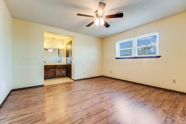 unfurnished bedroom featuring ensuite bathroom, a textured ceiling, baseboards, and wood finished floors